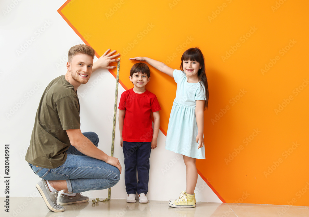 Father and his little children measuring height near wall