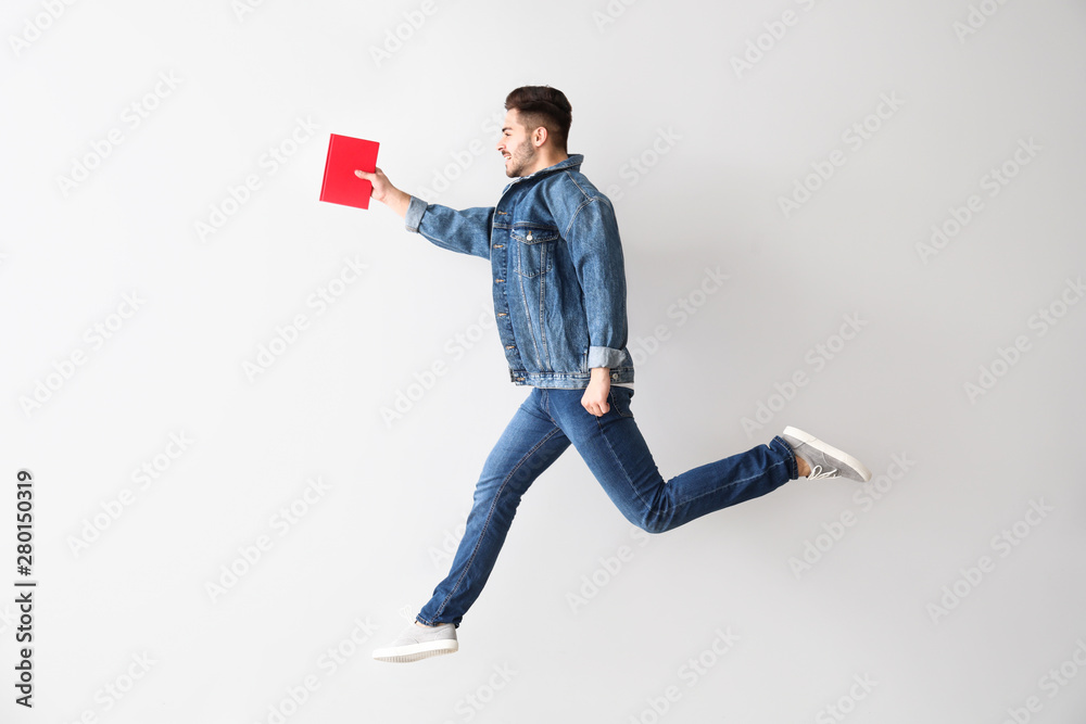 Jumping young man with book on light background