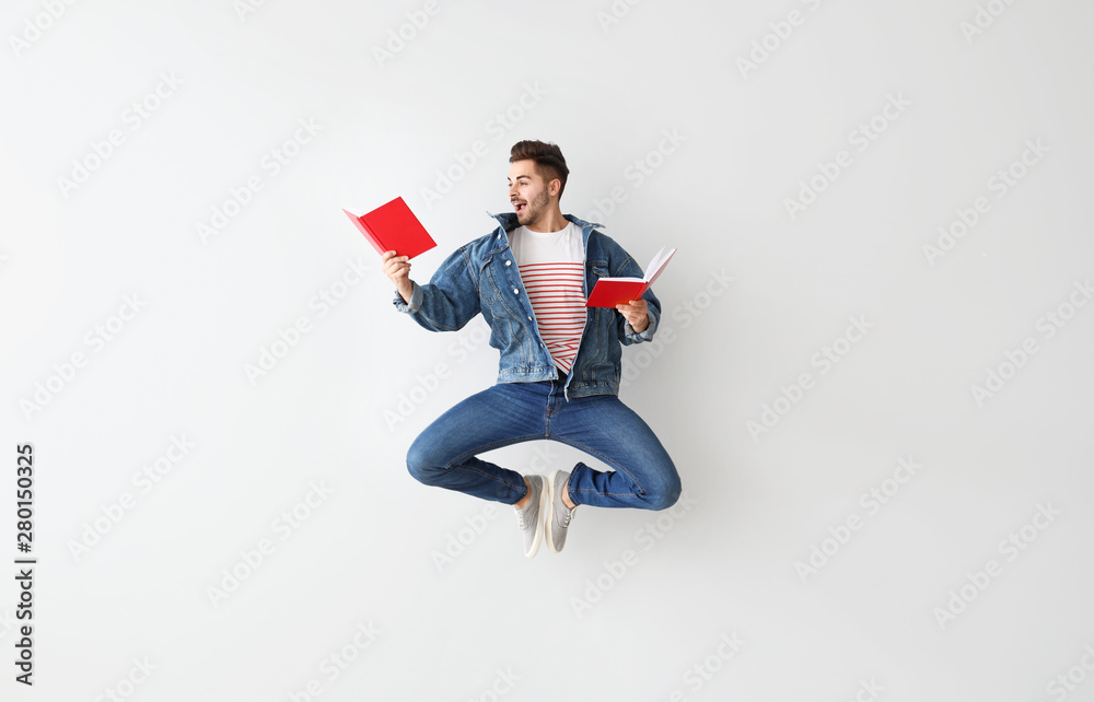 Jumping young man with books on light background