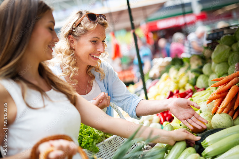 Young women friends baying vegetables and fruits on the market