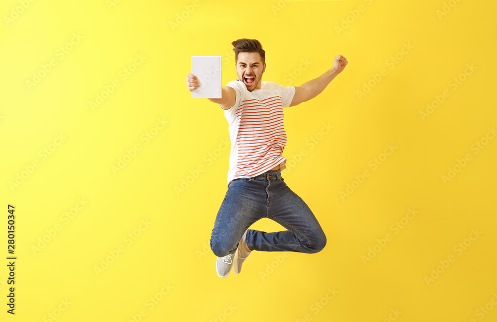 Jumping young man with book on color background