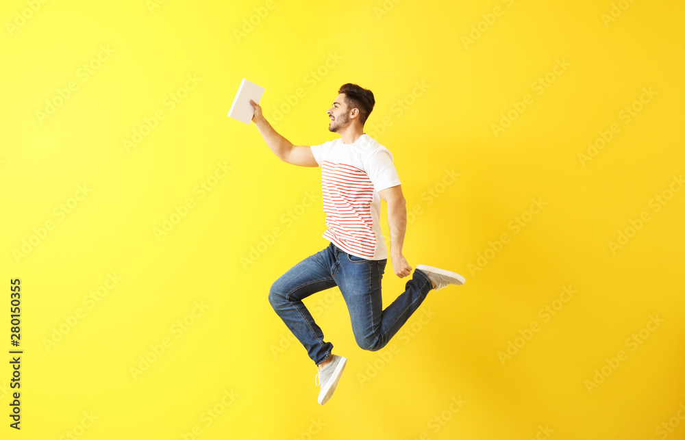 Jumping young man with book on color background