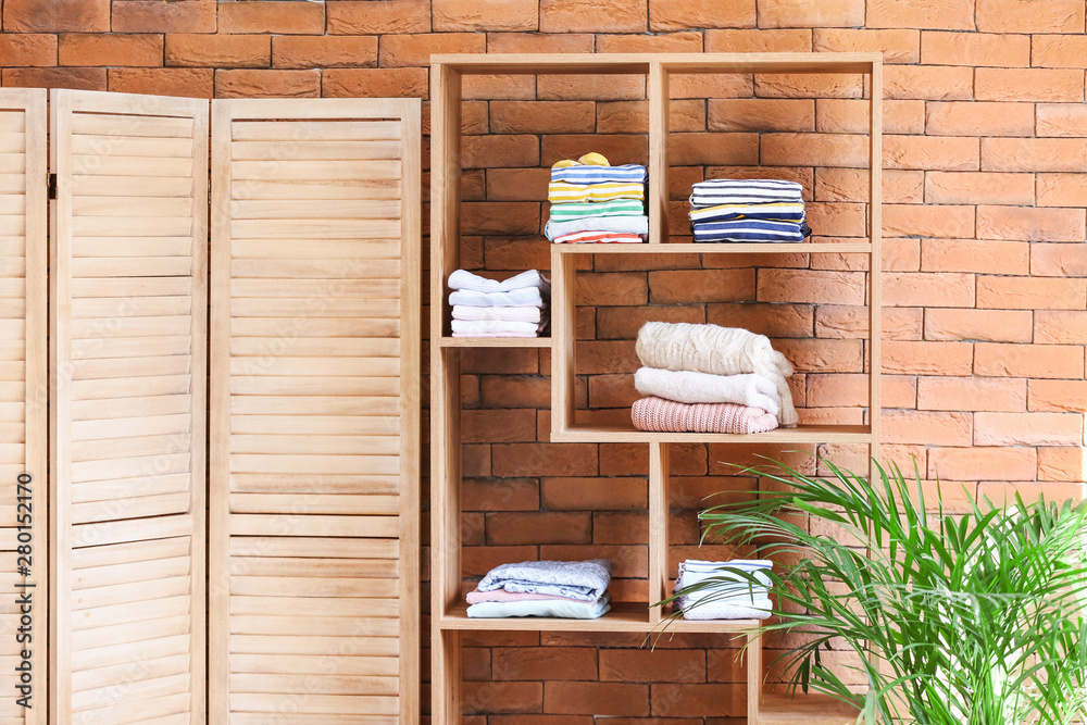 Rack with stacks of clean clothes near brick wall