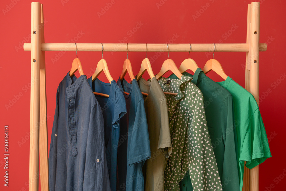 Rack with hanging clothes on color background