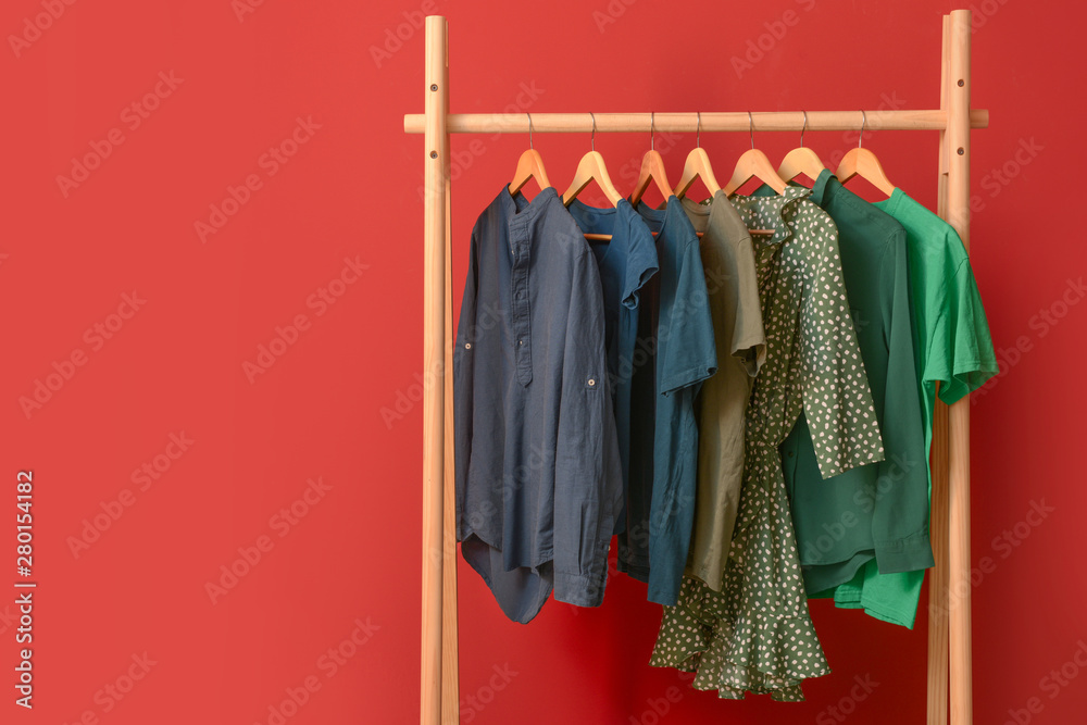 Rack with hanging clothes on color background