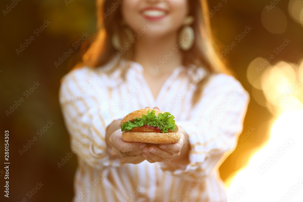 Beautiful young woman with tasty burger outdoors, closeup