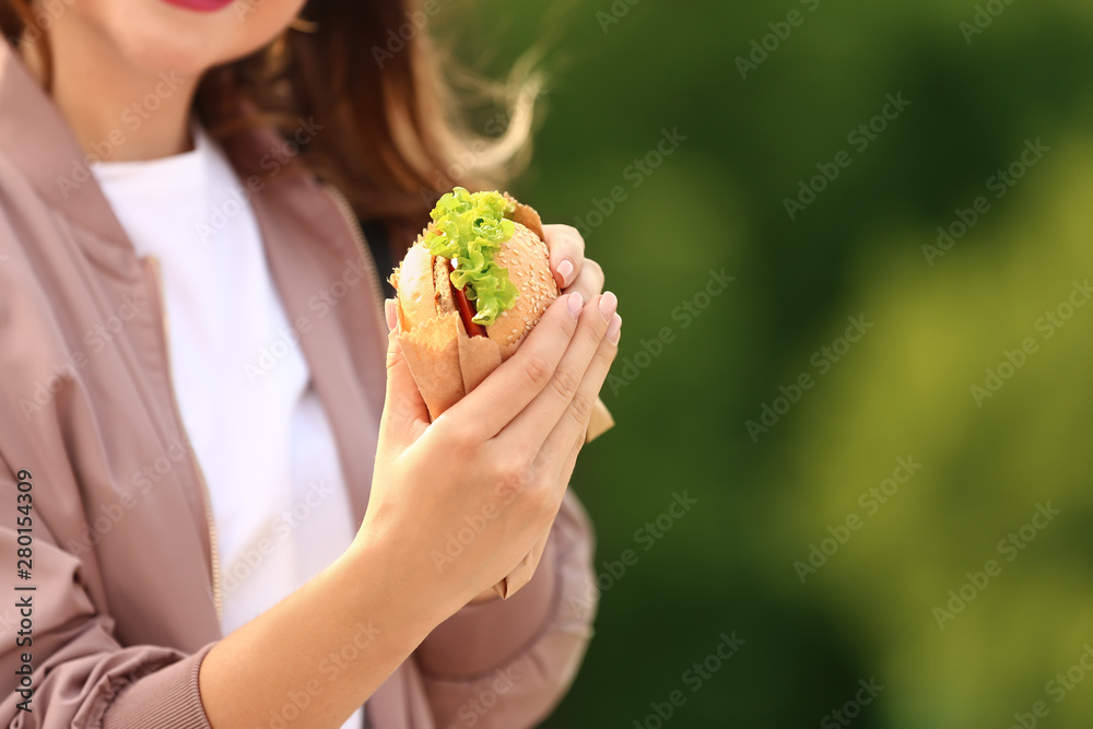 美丽的年轻女人在户外吃美味的汉堡