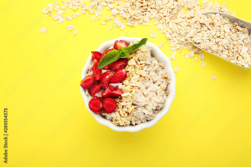 Bowl with tasty sweet oatmeal and scoop with flakes on color background