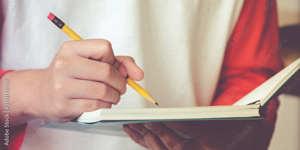 Close up of hand high school or university student in casual holding pencil writing on paper noteboo