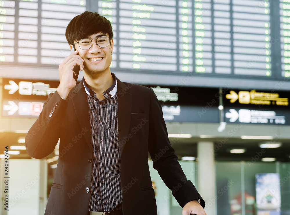 Elegant asian businessman checking email on mobile phone while walking with suitcase inside airport,