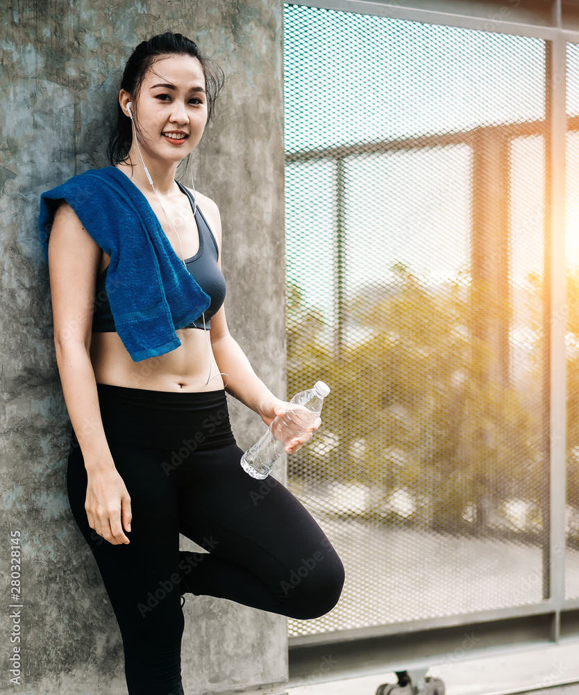 An beautiful Asian woman running, drinking water and listening music over road during moring. Workou