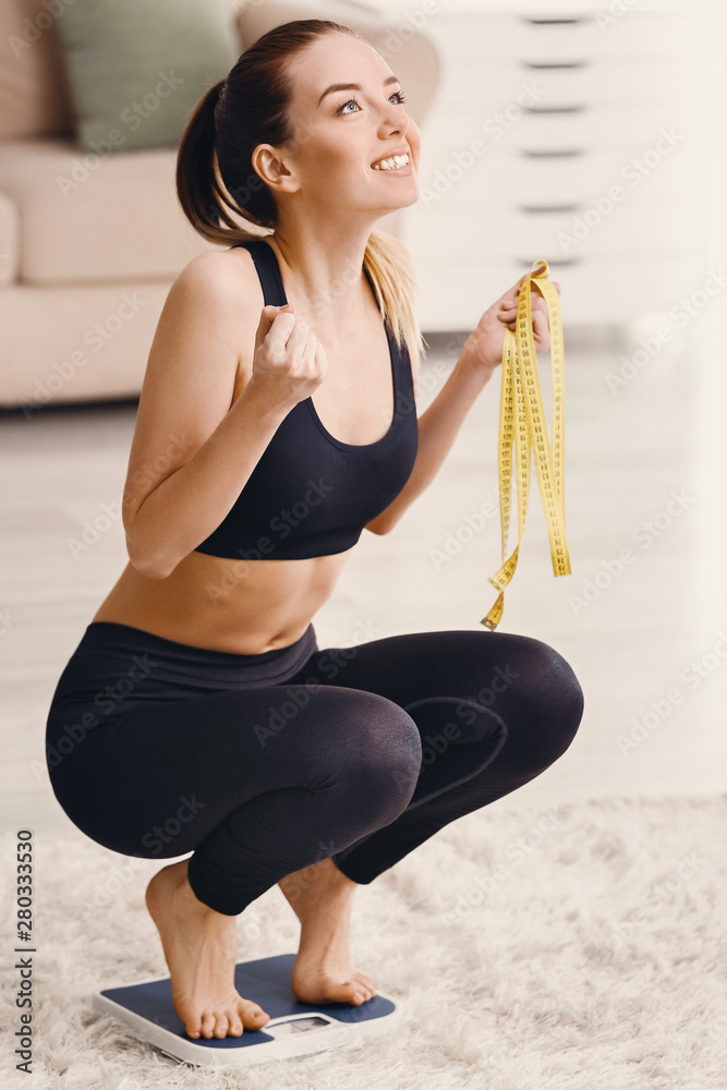 Happy young woman on scales at home. Weight loss concept