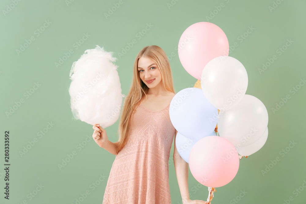 Beautiful woman with cotton candy and air balloons on color background