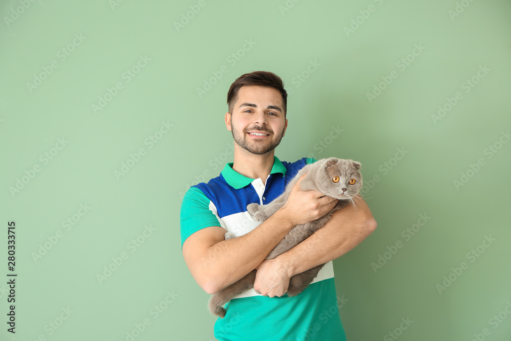 Young man with cute funny cat on color background