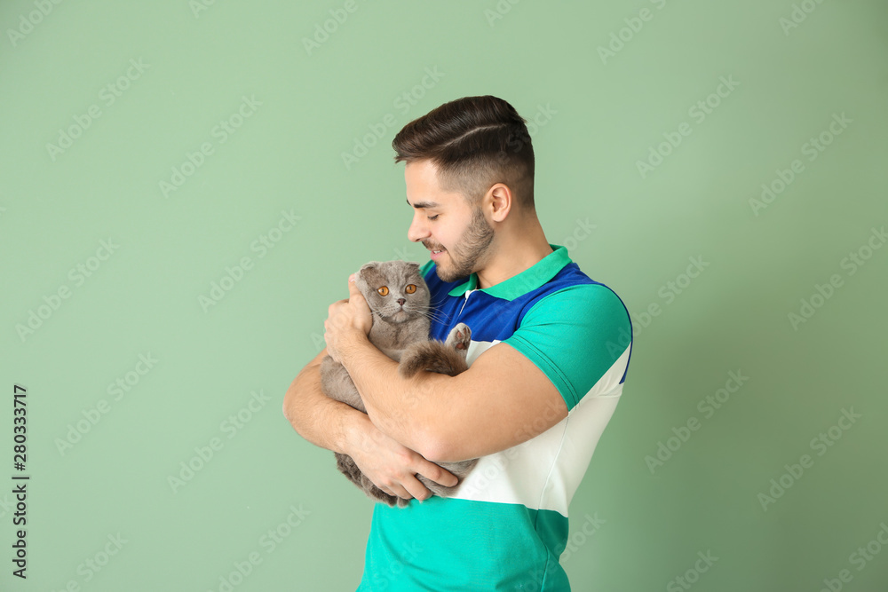 Young man with cute funny cat on color background