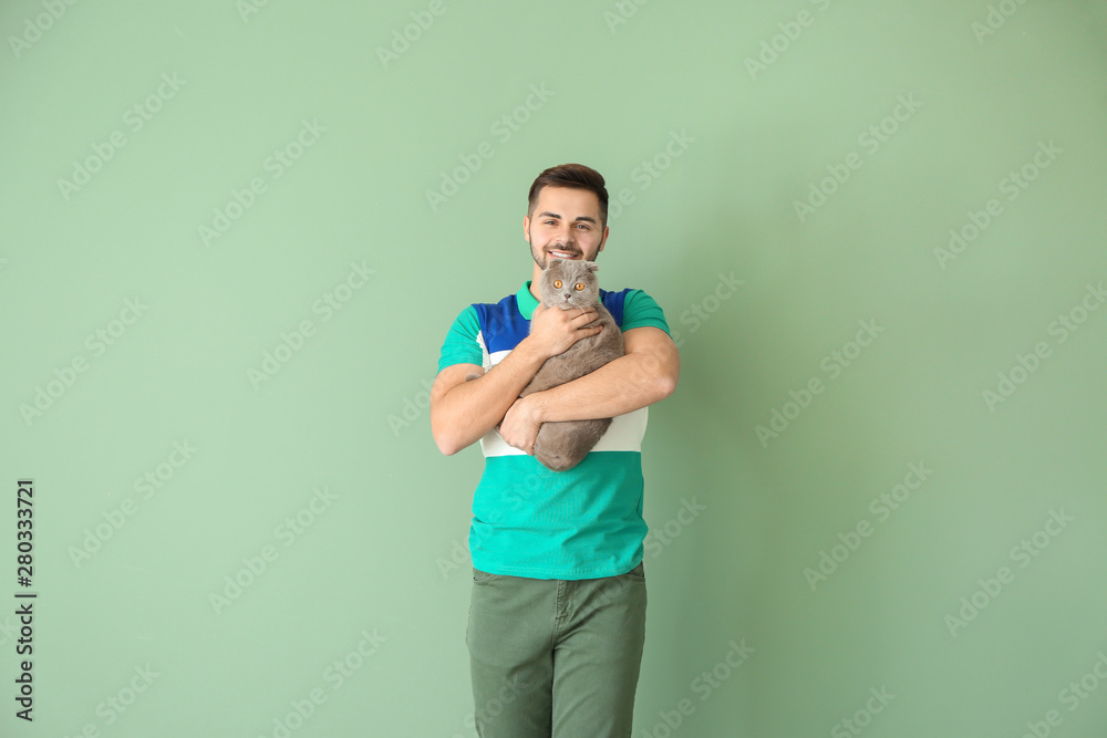 Young man with cute funny cat on color background