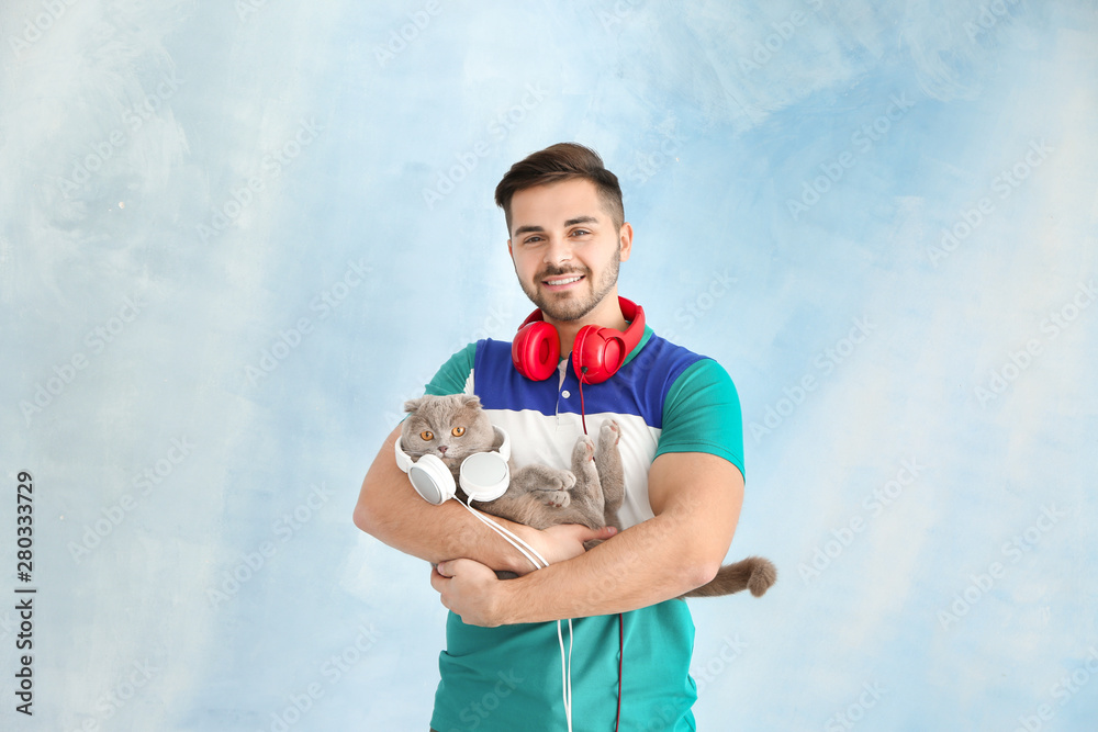 Young man and his cute funny cat with headphones on color background