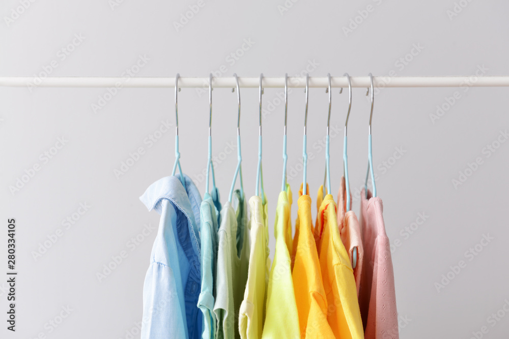 Stylish kid clothes hanging on rack against light background