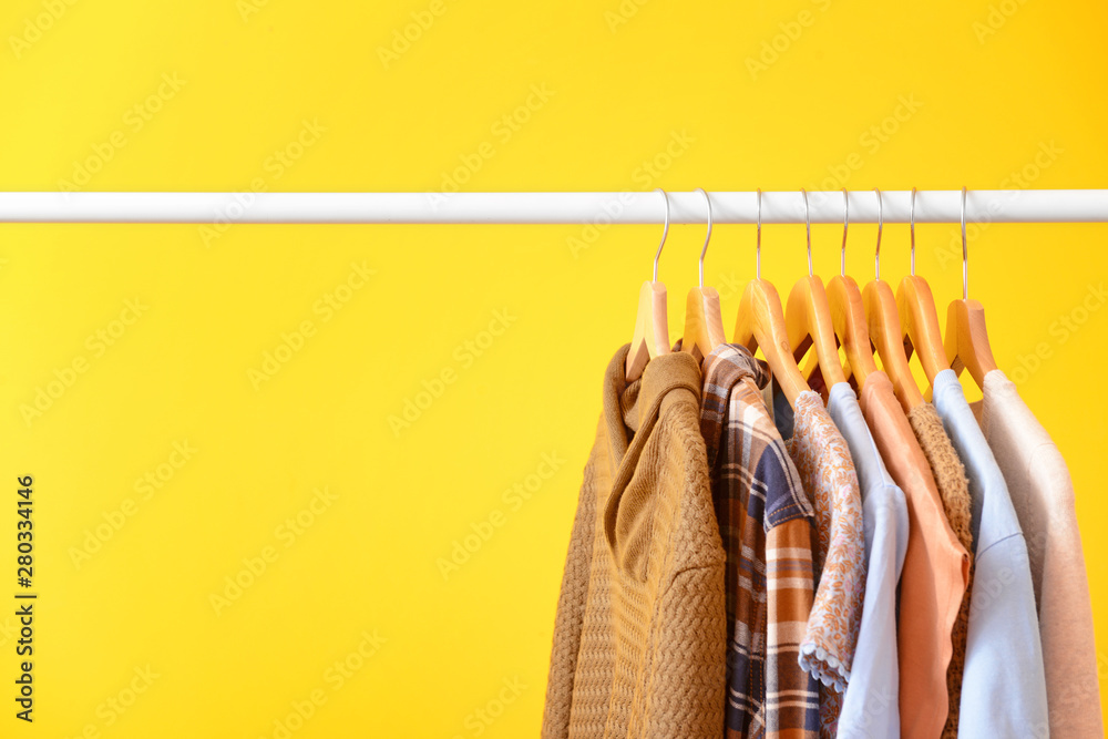 Rack with hanging clothes on color background