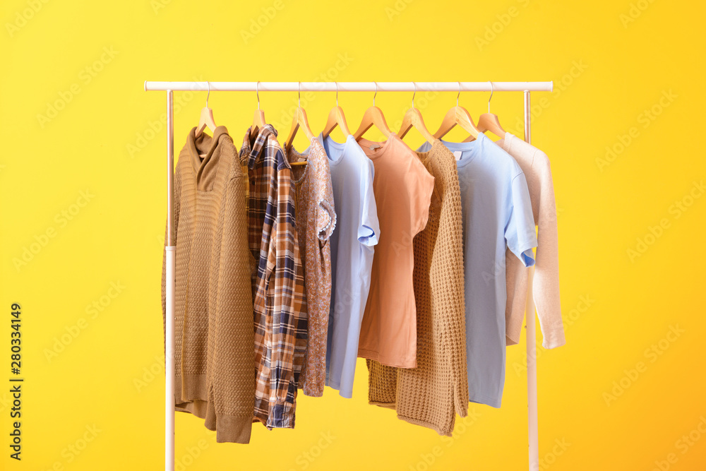 Rack with hanging clothes on color background