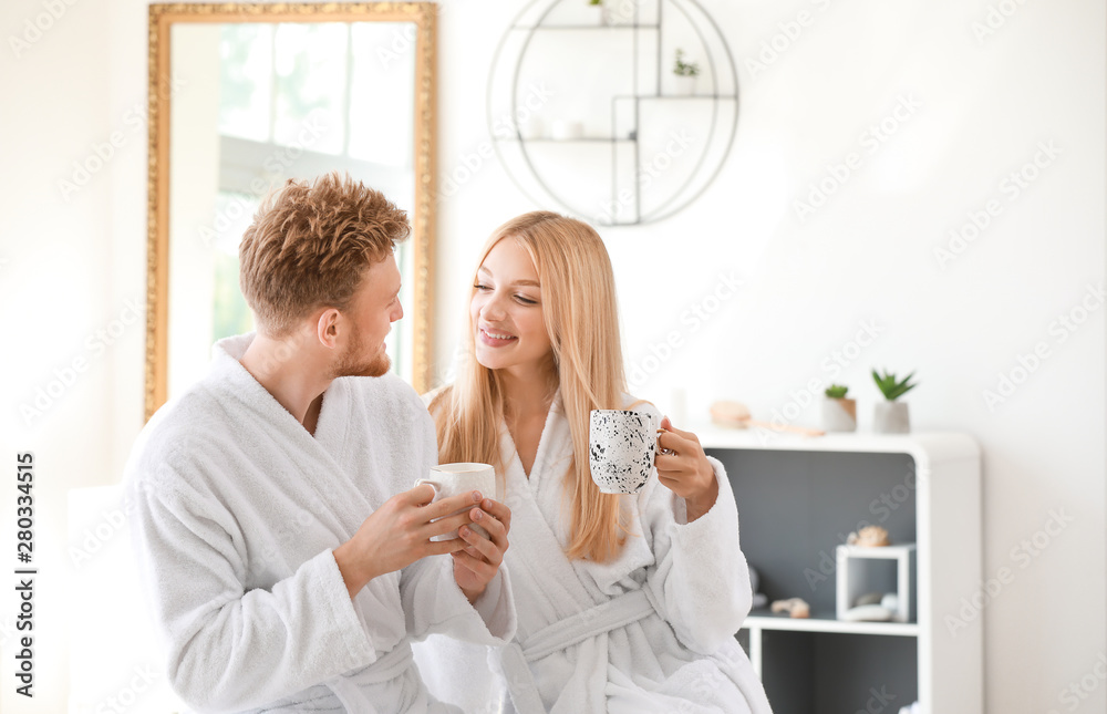 Morning of happy young couple in bathrobes drinking coffee at home