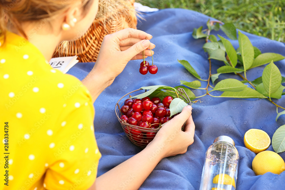 Woman with tasty fresh cherries in basket lying on plaid outdoors