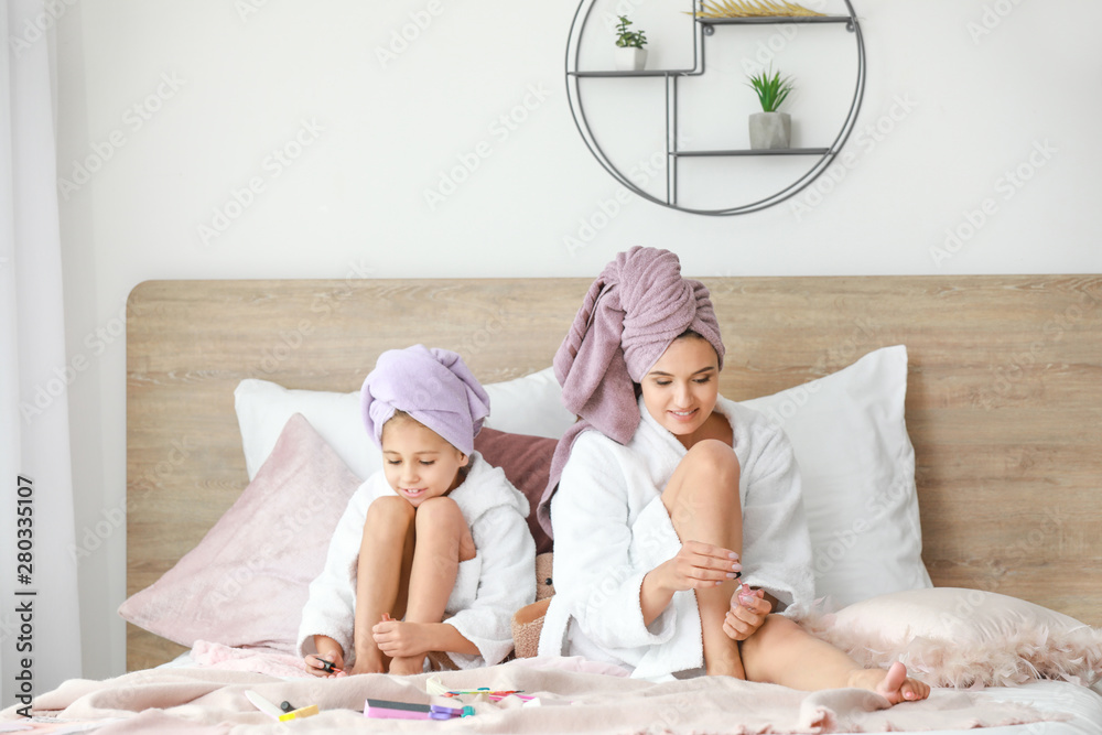 Mother and her little daughter in bathrobes doing pedicure in bedroom