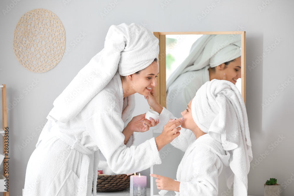 Mother and her little daughter in bathrobes applying facial cream at home