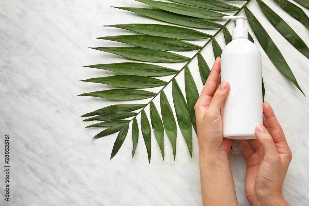 Female hands with cosmetic product and tropical leaf on light background