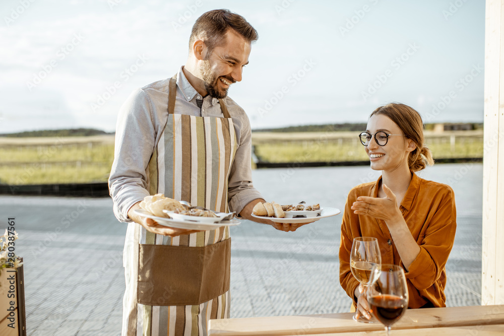 服务员在户外餐厅为一位年轻女性顾客端上美味的蜗牛馅菜肴