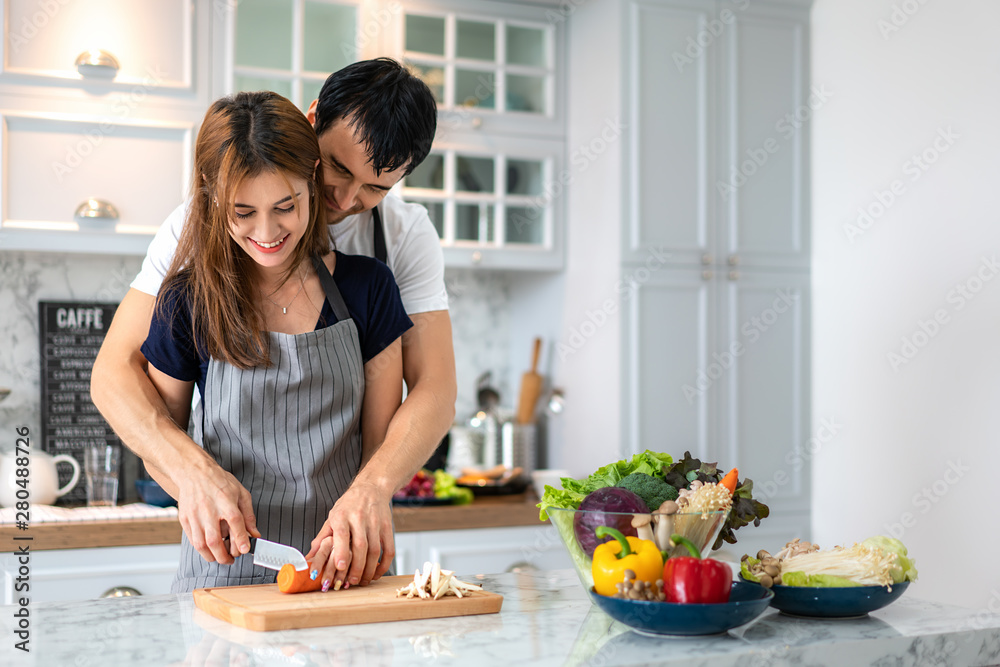 可爱的年轻夫妇在现代厨房准备健康的饭菜。早上男人拥抱女人浪漫