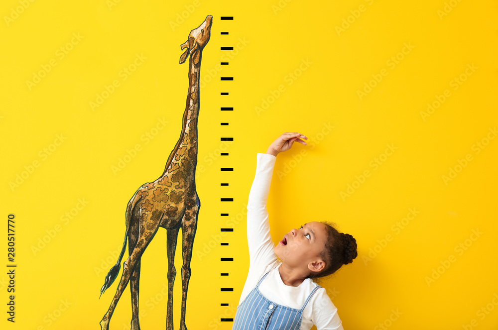 Surprised African-American girl measuring height near color wall with drawn giraffe