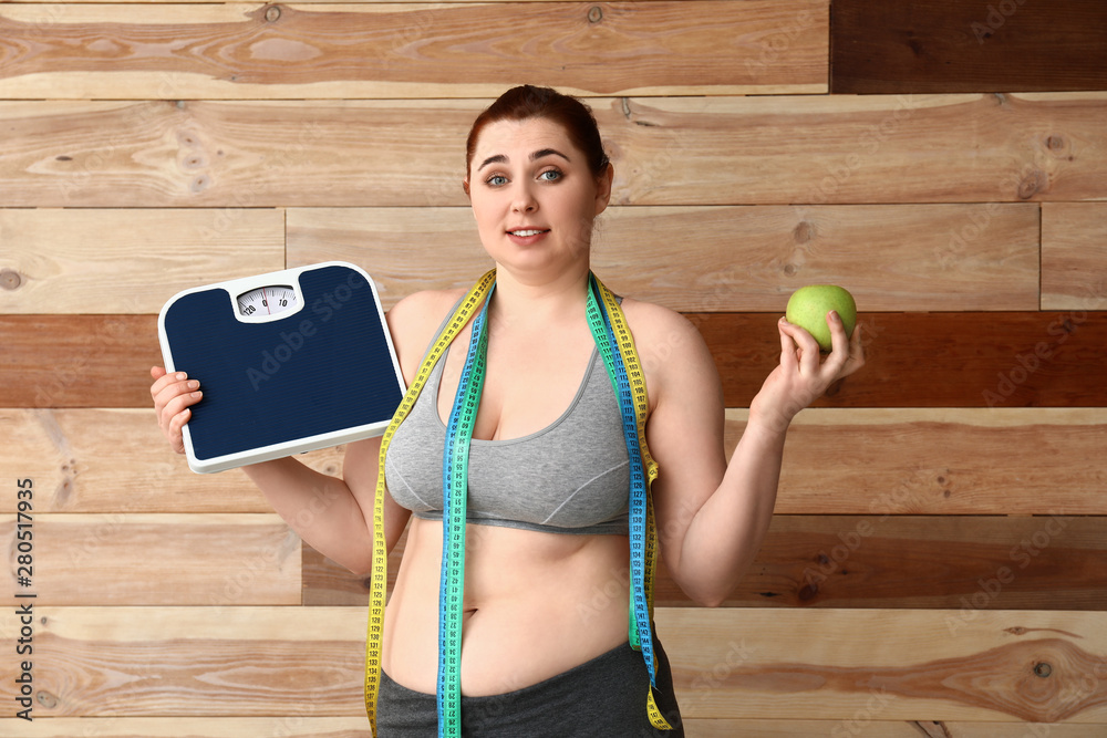 Overweight woman with scales, apple and measuring tapes on wooden background. Weight loss concept