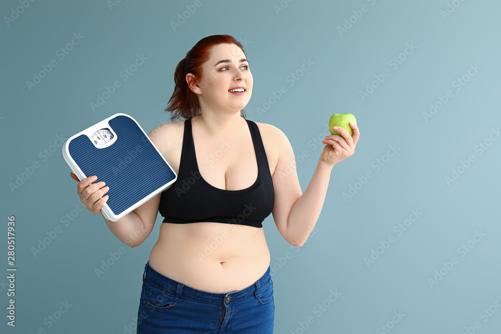 Overweight woman with scales and apple on color background. Weight loss concept