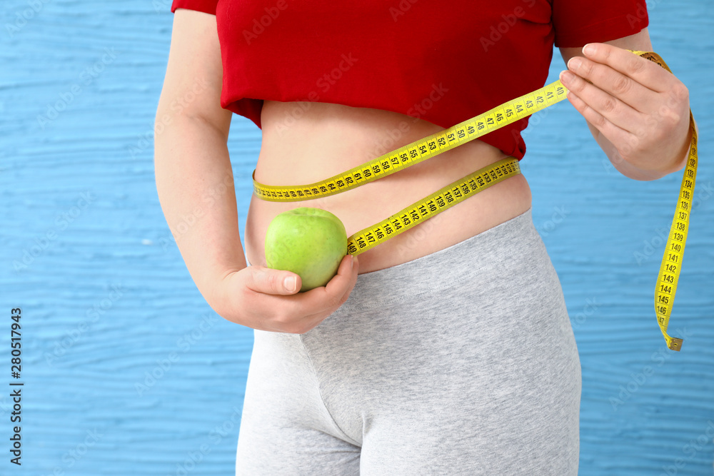 Overweight woman with apple and measuring tape on color background. Weight loss concept