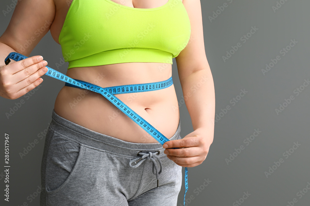 Overweight woman with measuring tape on grey background. Weight loss concept