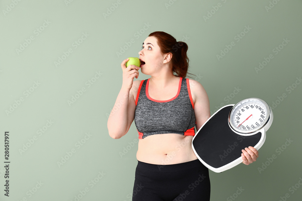 Overweight woman with scales and apple on color background. Weight loss concept