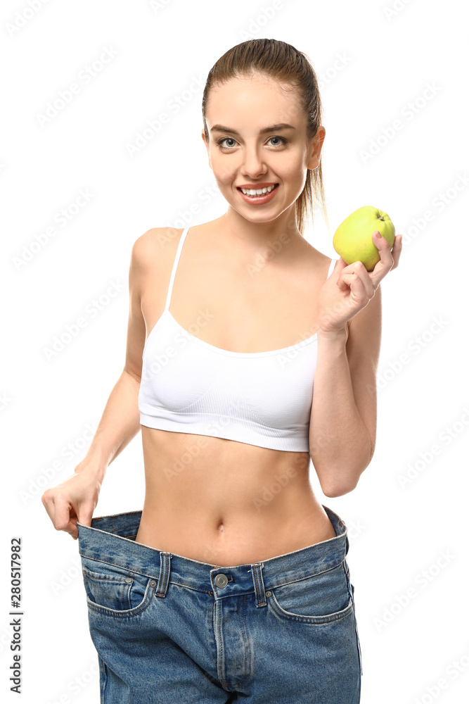 Happy young woman in loose jeans and with apple on white background. Weight loss concept