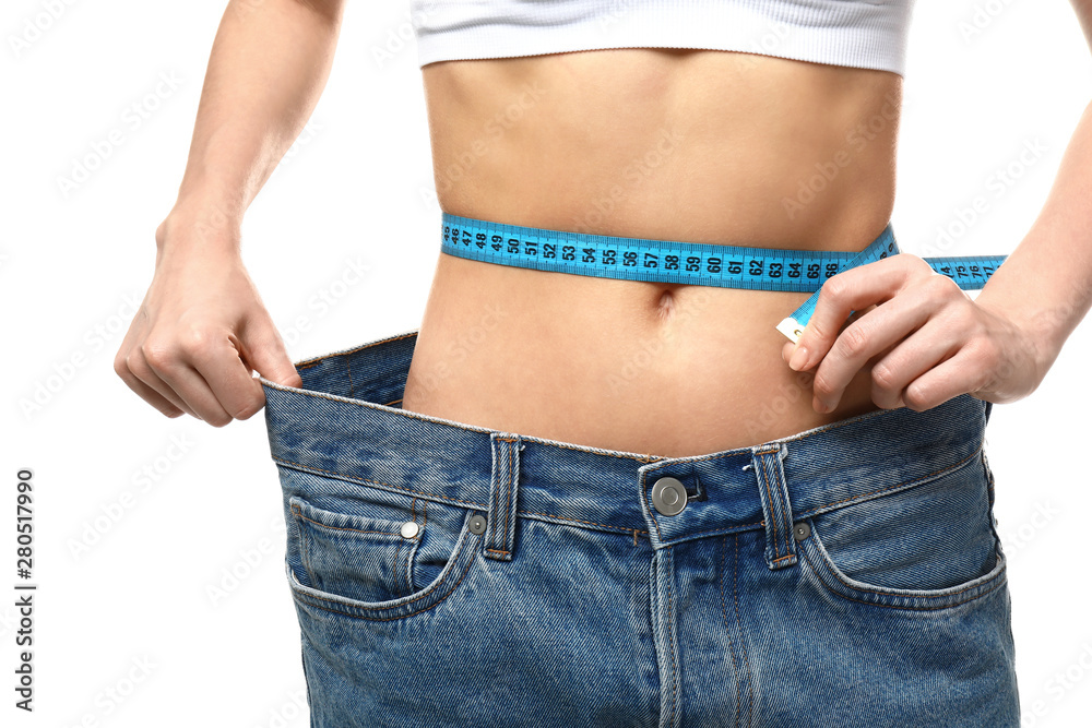 Young woman in loose jeans measuring her waist on white background. Weight loss concept