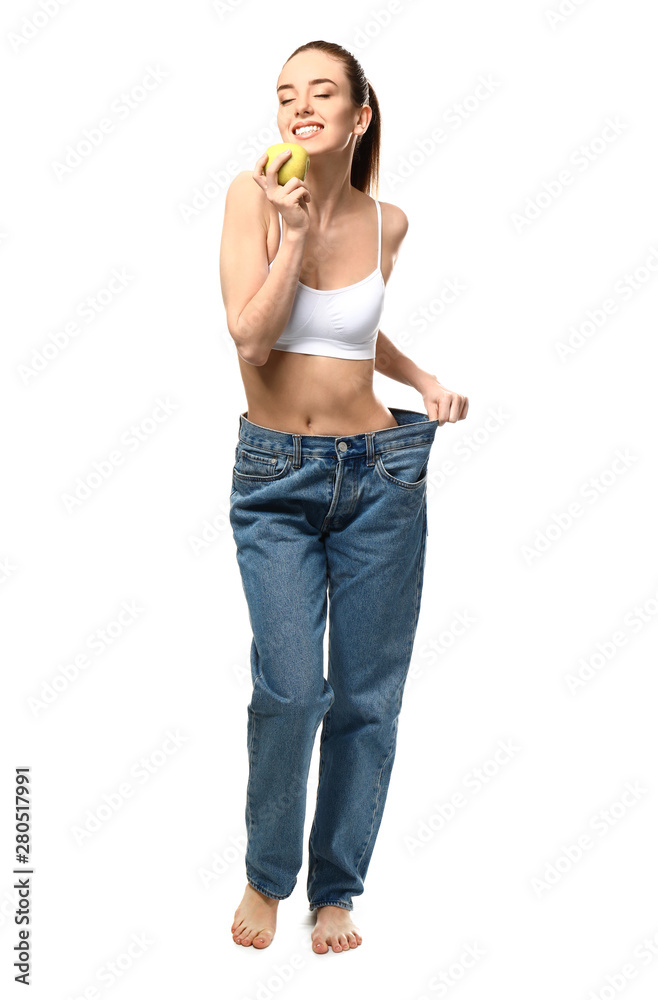 Happy young woman in loose jeans and with apple on white background. Weight loss concept