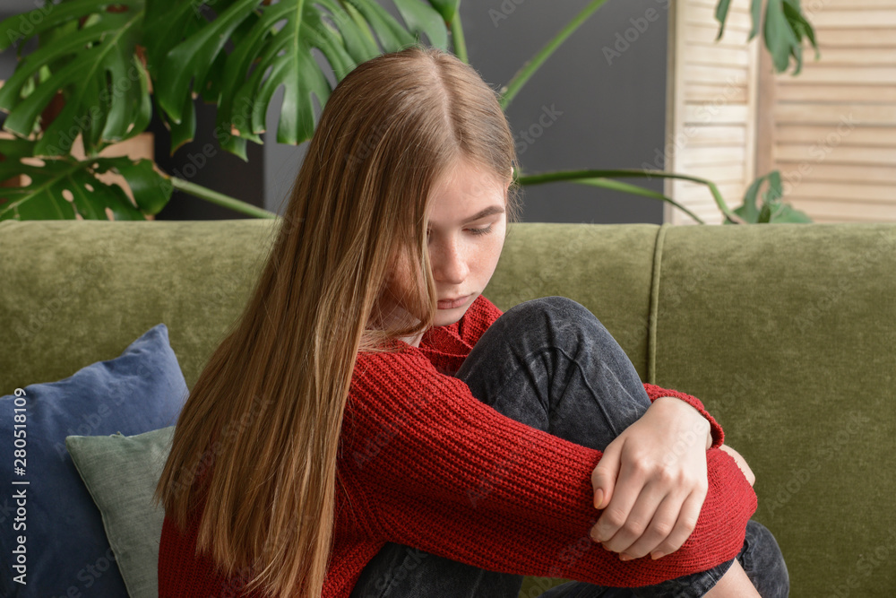 Sad teenage girl sitting on sofa at home