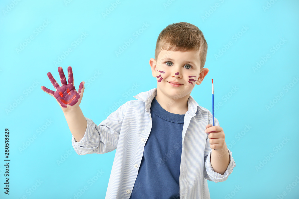 Funny little boy with hands and face in paint on color background