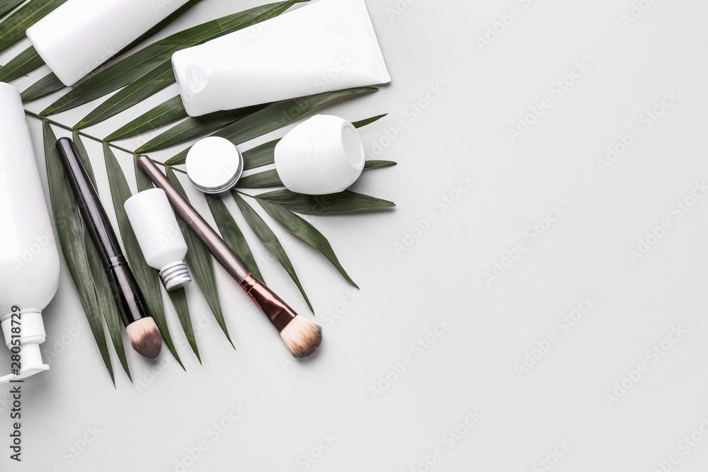 Set of cosmetic products and palm leaf on light background