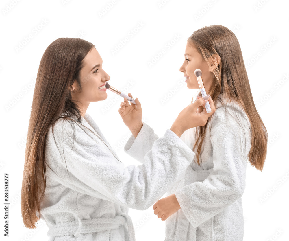 Mother and her little daughter in bathrobes applying makeup against white background