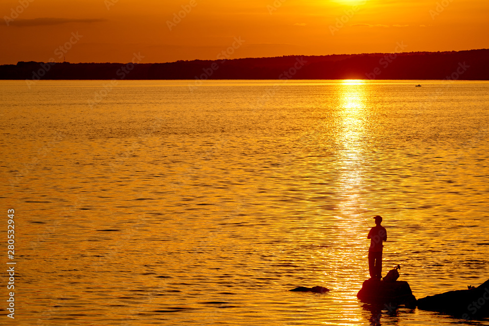 Fisherman on pier at sunset time. Beautiful sunset in the river and man with fishing rods.