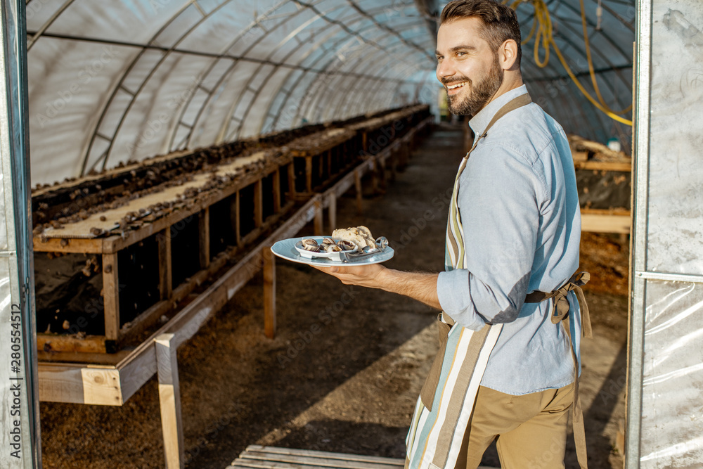 Portrait of a handsome chef cook standing with cooked snails in the hothouse of a farm for growing s