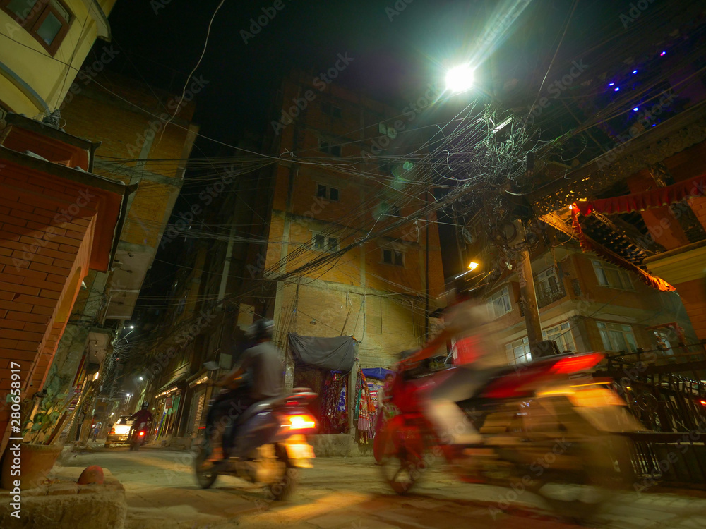 低角度：加德满都当地人在夜间沿着小巷骑着滑板车