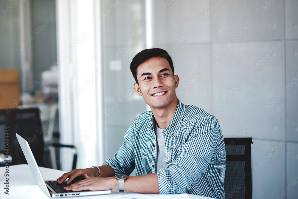 Happy Young Businessman Working on Computer Laptop in Office. Smiling and looking away