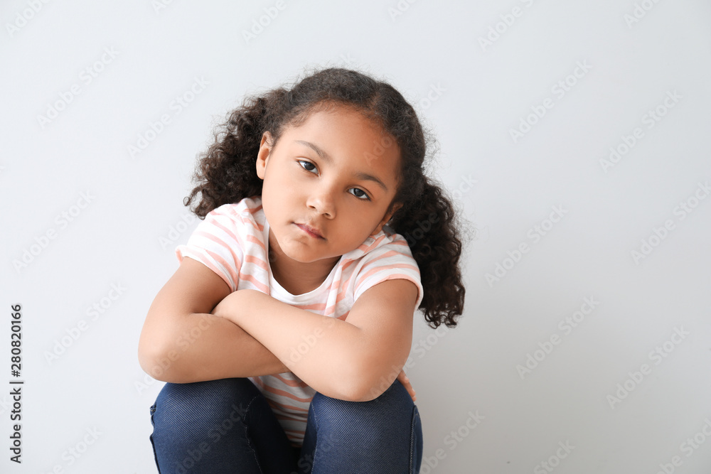 Portrait of sad little African-American girl on light background