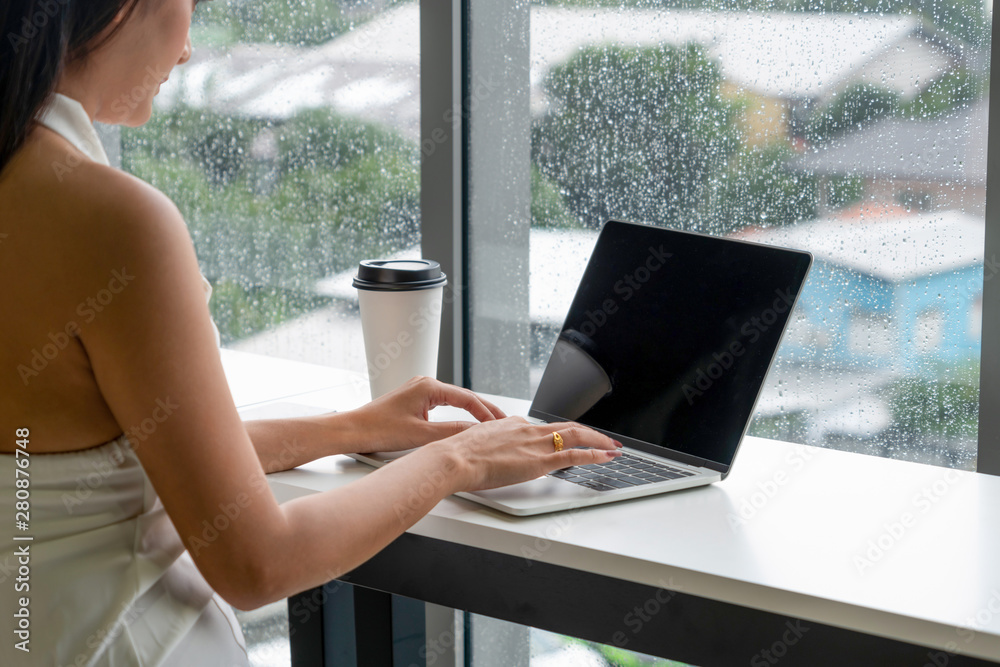 Young business woman using laptop computer while sitting at cafe table next to office windows.